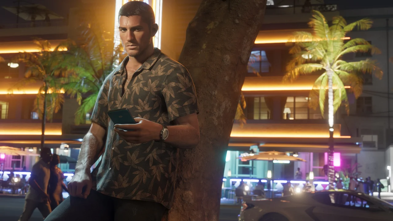 Man holding a phone beside a tree on a palm-lined street at night